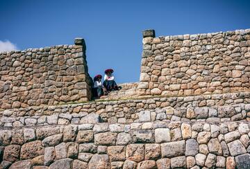 Two native women sit atop a rock wall in Peru.