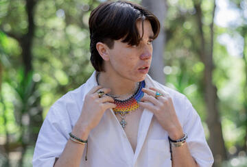 Anagali Ducan adjusting a colorful beaded necklace while standing outdoors with greenery in background.