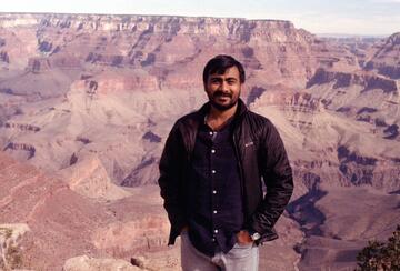 Image of Humzah Khan in a brown jacket, posing in front of the Grand Canyon