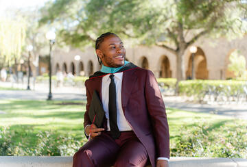 MIP Student Tyler smith posing in a suit and graduation hood in front of a Stanford building recognizable by its arches