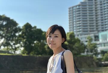 Image of MIP student Yukiko Ueda in a a white tank top with trees and buildings in the background
