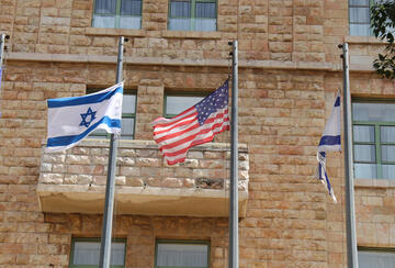 Israeli and American flags flying in front of brick building in Jerusalem.