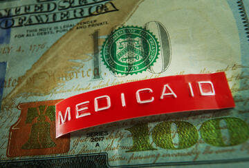 Photo illustration of Medicaid label on top of a U.S. dollar