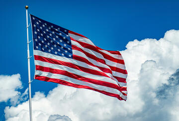 An American flag flying from a white pole against a bright blue sky with large white clouds.