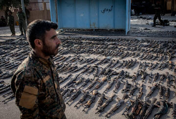 An SDF (Syrian Democratic Forces) fighter looks over seized ISIL weapons