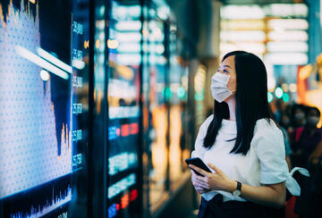 Woman in a face mask looking at a stock market board