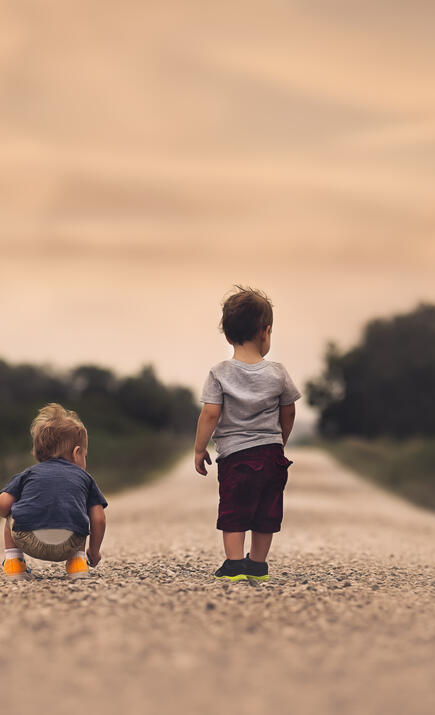 Two toddlers walking down a dirt road
