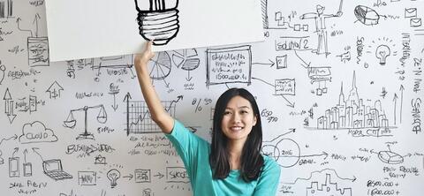 seated young woman holding a drawing of a light bulb