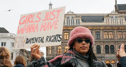 Woman in black jacket and pink hat holding sign at march