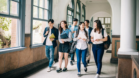 A group of Asian college students what down a sunny hallway. 