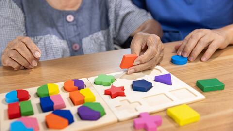 Close-up on an elderly womna's hands holding colorful puzzle pieces.