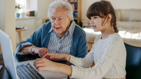 grandmother with child who is helping grandma use a laptop placed on a desk