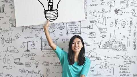 seated young woman holding a drawing of a light bulb
