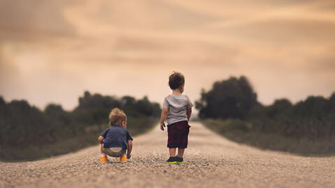 Two toddlers walking down a dirt road