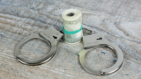 A pair of handcuffs next to a roll of paper money bills.