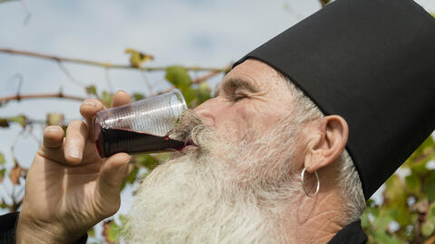 A senior orthodox priest with white beard enjoying a glass of red wine.