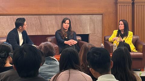 Three speakers during a panel discussion, seated on stage in the Bechtel Conference Center, Stanford University.