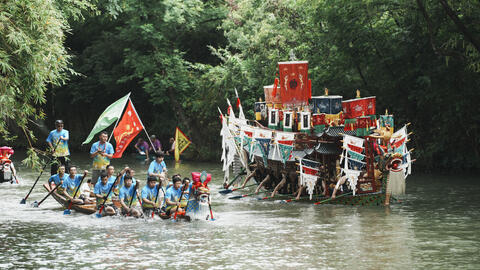 A boat and dragon boat being rowed by men go down a river in China.