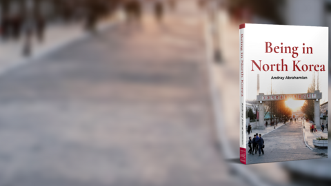 Cover of the book Being in North Korea on the background of a road with blurred figures walking