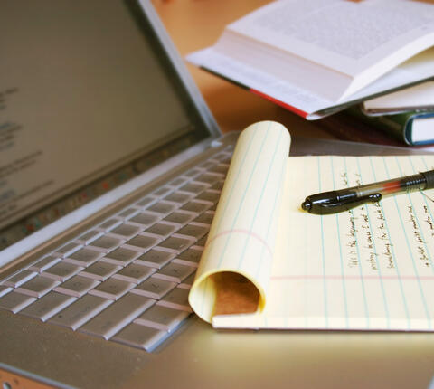 Laptop computer with books, pen and yellow legal pad