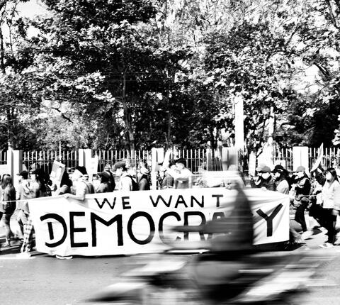 Democracy protest in Myanmar, protesters carrying sign reading "WE WANT DEMOCRACY"