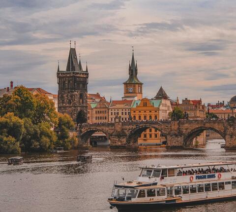 View of Prague's Charles Bridge and Old Town skyline over the Vltava River, with a tour boat in the foreground.