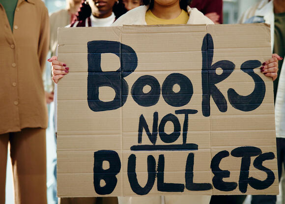 An image of students holding a protest sign that reads "Books not bullets" 