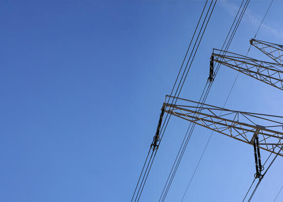 Looking up steel power pylon construction with high voltage cables against blue sky