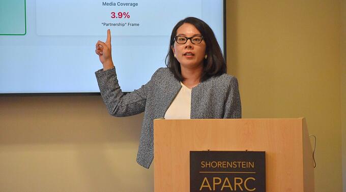 Xinru Ma presenting from a lectern, poninting to a screen behind her.