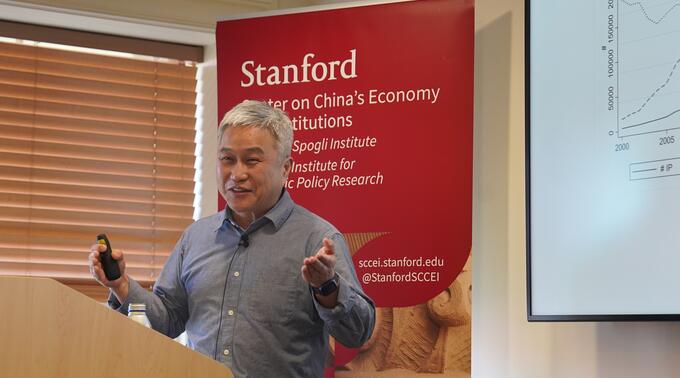 Hanming Fang presents in front of slides in a conference room.