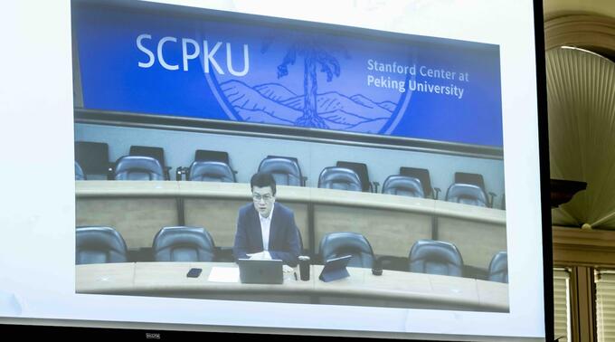 Speaking via video link from the Stanford Center at Peking University, Da Wei is shown on a screen.