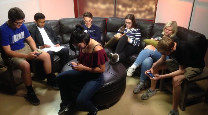 Photo of several teenagers on a couch with some looking at cell phones