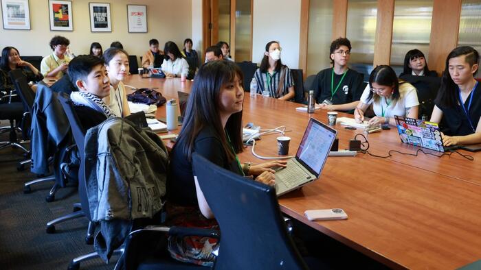 Participants in a discussion seated around a long table in a conference room.