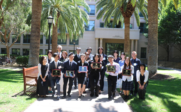 people with plaques are gathered outside in front of palm trees