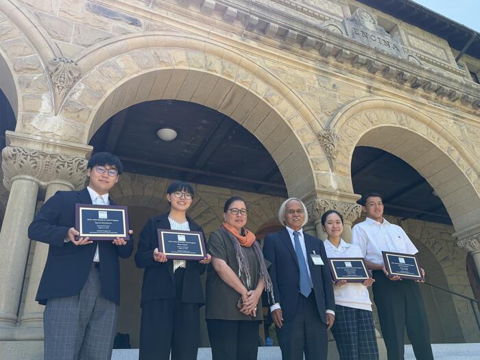 students with plaques standing outside of Encina Hall at Stanford