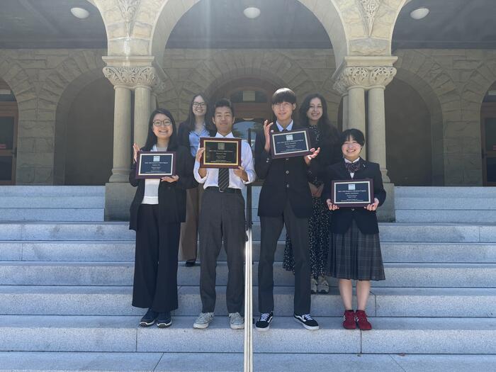 students with plaques standing outside of Encina Hall at Stanford