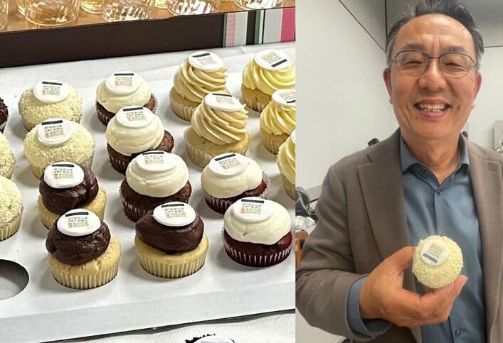 A tray of cupcakes decorated with the cover design of the book "The Four Talent Giants" and a photo of Gi-Wook Shin holding one of those cupcakes while similing to the camera.