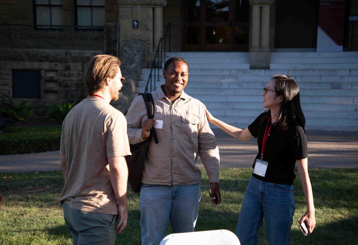 Three alumni of the Ford Dorsey Master's in International Policy chat near the steps of Encina Hall at Stanford University.
