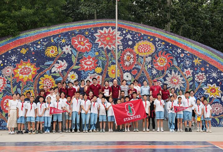 Photo of school kids and university students in front of a mosaic wall.