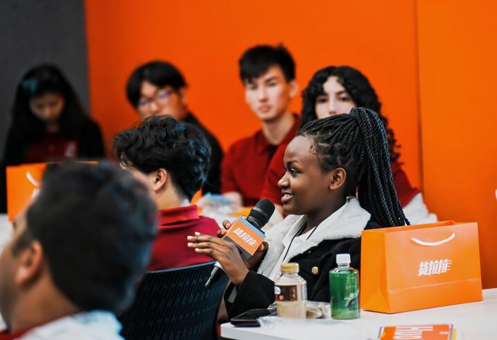 Student speaks into a microphone in an orange conference room.