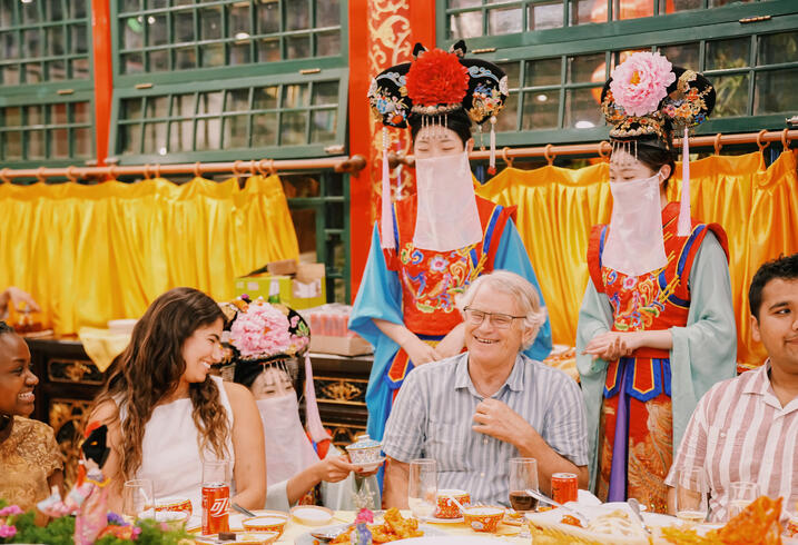 Scott Rozelle and students eat in a colorful restaurant in China with a woman dressed as a geisha behind.