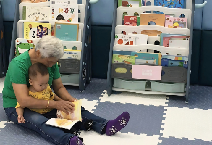 A grandparent holds a child in their lap and reads to them.