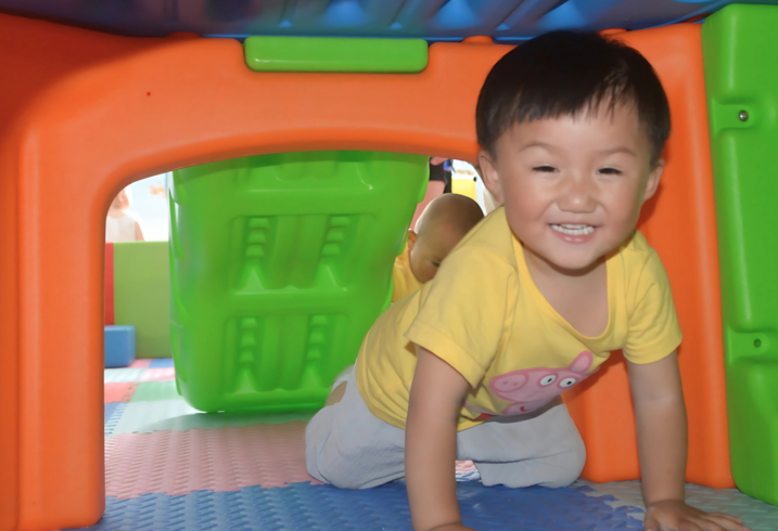 A toddler crawls through a colorful play structure. 