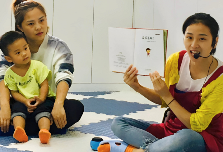 A staff member at a parenting center reads a book aloud to a child and caregiver.