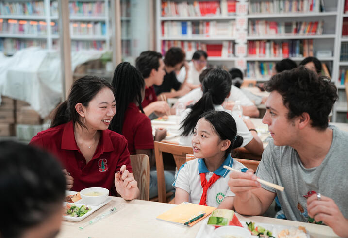 College students chat with young school children in classroom.