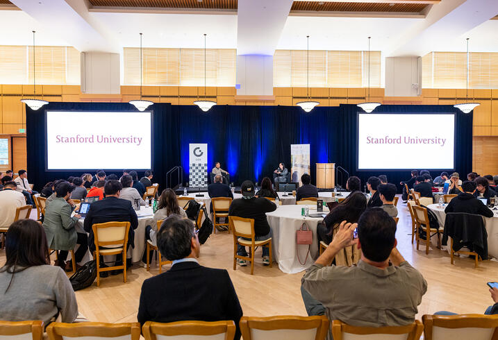 Event attendees seated at round tables listening to a fireside chat.