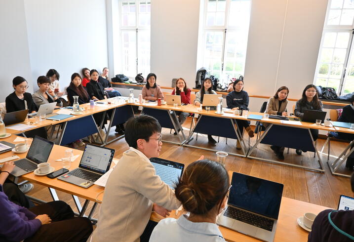 A group of people with open laptops sit around a square table.