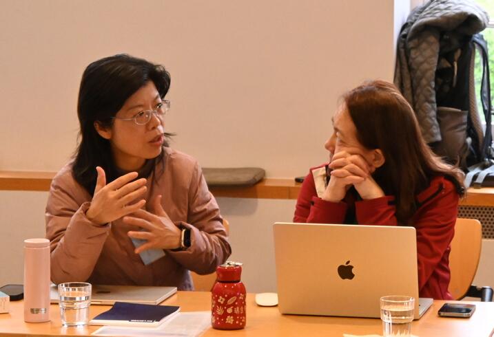 Women sit at a table and engage in conversation during a conference session.