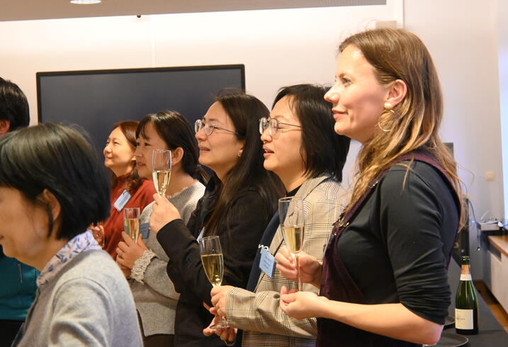People stand with champagne glasses listening to a speech at a reception.