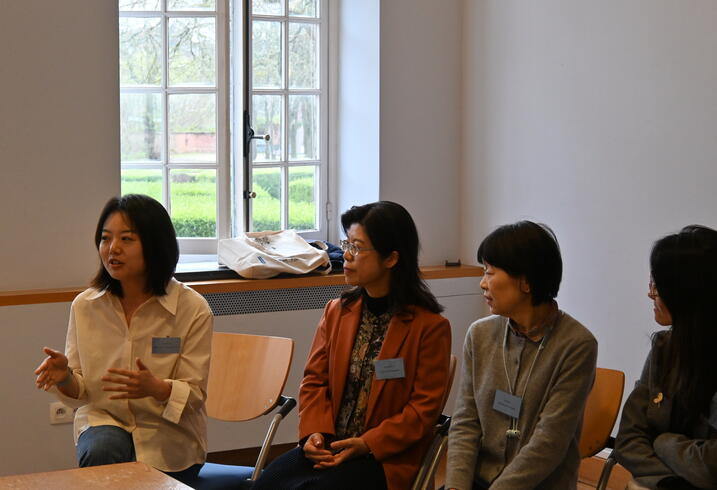 Women sit at a table and engage in conversation during a conference session.